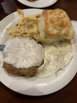 Country fried steak, fried eggs, hash brown casserole and a biscuit.