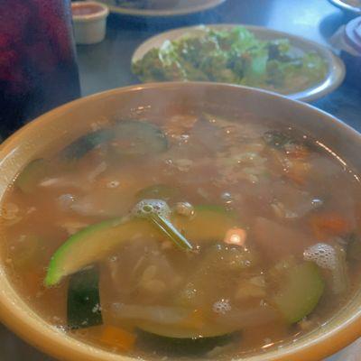 Tortilla soup with some guacamole behind it