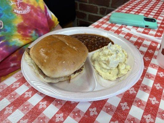 Beef brisket sandwich with side of potato salad and beans