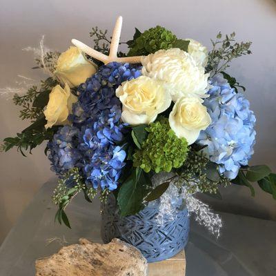 Hydrangea and roses with a sea star in a classic blue pottery is a signature drinkwater arrangement called Nantucket Beach.