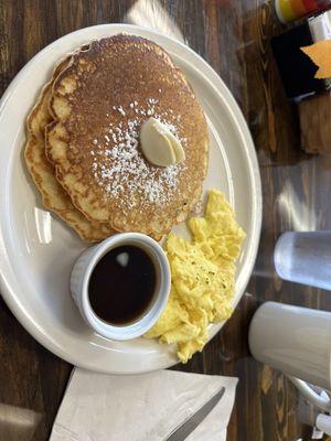 Pancakes and scrambled eggs with a side of maple syrup.