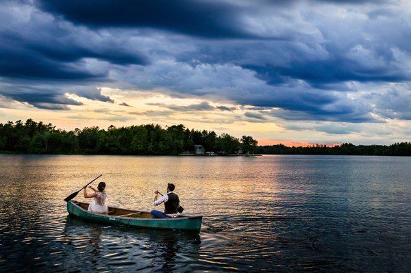 A bride and groom row on a canoe at sunset at their lakeside Maine wedding. Photo by Kate Crabtree Photography.