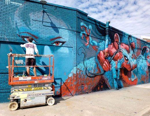 Mural artist using WACO scissor lift for Plaza Walls Mural Expo 2019