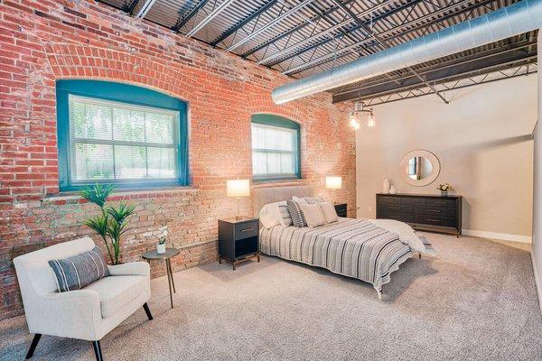 A bedroom with industrial brick walls and two large windows at Wireworks Lofts in the Square.