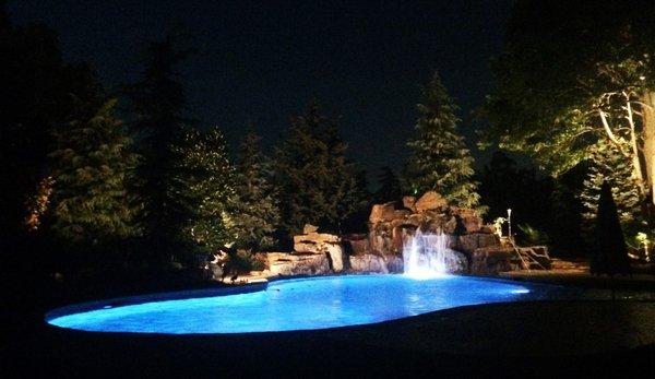 Landscape lights softly illuminating landscape behind a pool in oklahoma city (okc) by Scapes, inc.