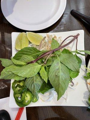 Fresh condiments for pho: lots of basil, crunchy sprouts, jalapeño slices, and limes.