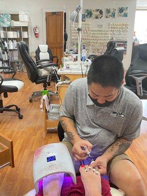 Nail tech doing his thing, with second color wall in background.