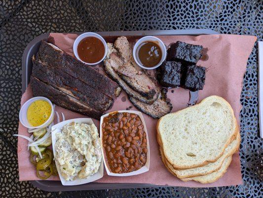 Three meat plate with burnt ends, brisket, and spare ribs. Plus, baked beans, potato salad, and saucy sides.