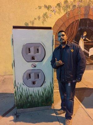 A team member posing next to control box painted  as an outlet.