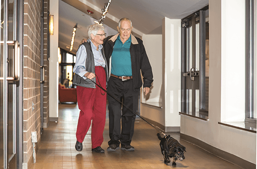 Happy couple with their dog walking the hall at Kavod Senior Life.