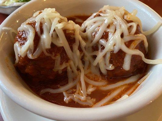 Two meatballs in a bowl with cheese