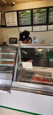 Employee whose hair is hanging in the food area while he leans over the serving area.