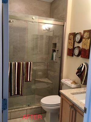 New bathroom after renovation with barn-door shower doors, full wall and floor tiles, niche, grab bars