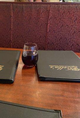 A table with some menus and a glass of wine.