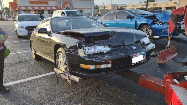 Before repair - on wrecker - damage to hood, fender, bumper and upper bulkhead