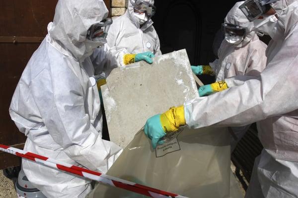 Properly protected asbestos workers bagging contaminated materials into properly labeled bags.