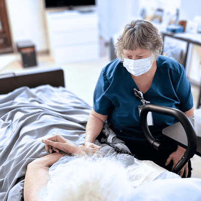 Noble Hospice CNA sitting bedside with a patient.