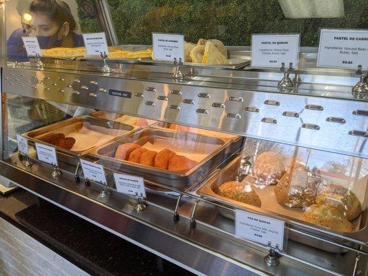 Hot food case with some common salgadinhos (i.e. pão de queijo, risole, empadinha). There's another case with desserts