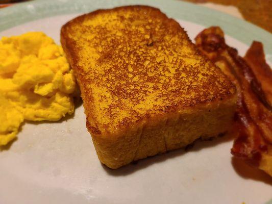 Close up of French toast with eggs and bacon.