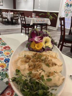 Potato pierogi with fancy garnishes that look like flowers plus an orchid flower, with other, empty tables in the background.