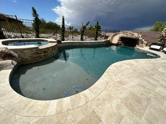 Finished pool with rock feature and travertine decking.