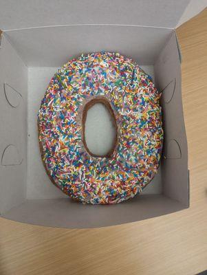 Extra large donut in a box that normally holds a dozen donuts.