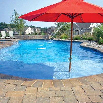 Free-form concrete pool with brick coping, laminar deck jets, and tanning ledge with integrated sun umbrella