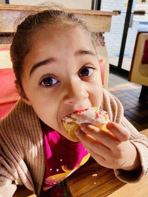 Customer enjoying vanilla iced donut with sprinkles