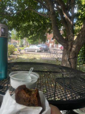 I am sitting under a tree at a table outside with some banana bread and Chia pudding