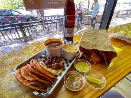 Two Birria tacos with an Al Pastor, consommé, queso & chips, with a Mexican Coke.