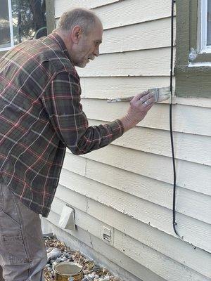 Focused on his work fixing siding and painting it the same color as rest.