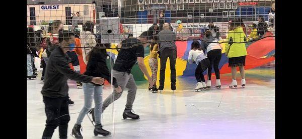 The parachute game in the middle of the rink and people skating on the outside.