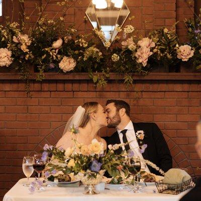 Our sweetheart table with repurposed ceremony florals behind us on the fireplace