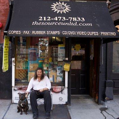 The Source Unltd Print & Copy Shop NYC owner Santo sitting in front of his business with his best friend Clyde