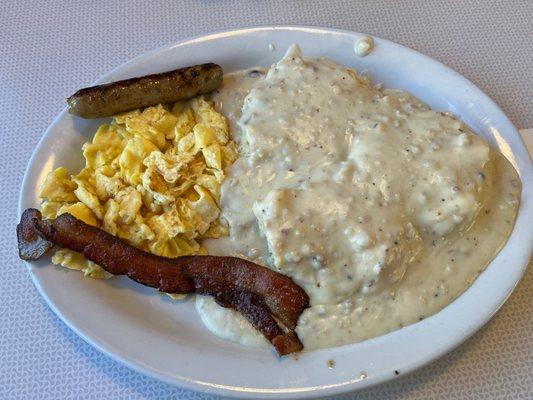 Biscuits and gravy with two scrambled eggs, bacon, and a sausage link.