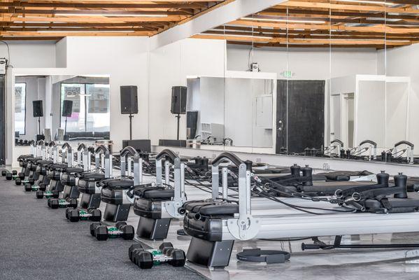 The Sweat Pilates studio features reformer machines and heavy weights, arranged neatly for a clean and functional workout space.