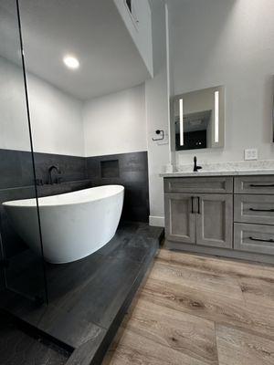 Ash brown vanity with quartz countertops, porcelain tile shower walls and luxury vinyl floor. Matte black hardware frameless shower panels.