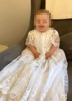 Small child in custom lace christening gown sitting in a grey chair.