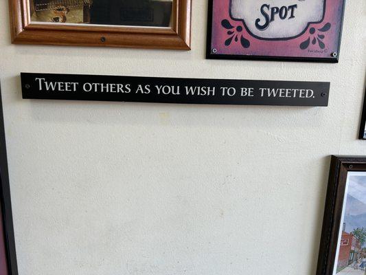 Narrow horizontal black sign with white letters that says: "Tweet others as you wish to be tweeted."