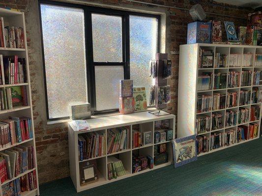 Back wall of books with a stained glass window letting in lots of sunlight.