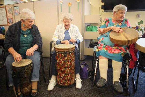 Three elderly women playing drums together at a local community center - promoting their cognitive, social & emotional wellbeing!