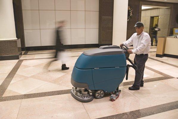 Worker cleaning granite floor with a auto scrubber.