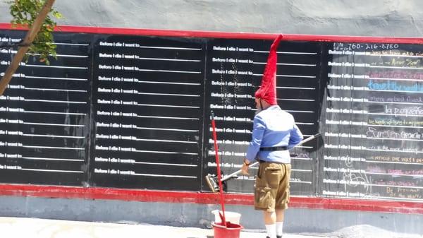 Outside wall "Before I die, I want to ____" chalkboard being cleaned by your friendly Gnome.