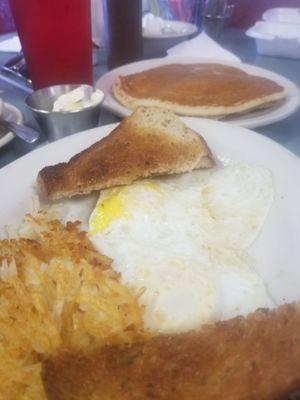 Two eggs over medium , hash browns, rye toast and one blueberry pancake.