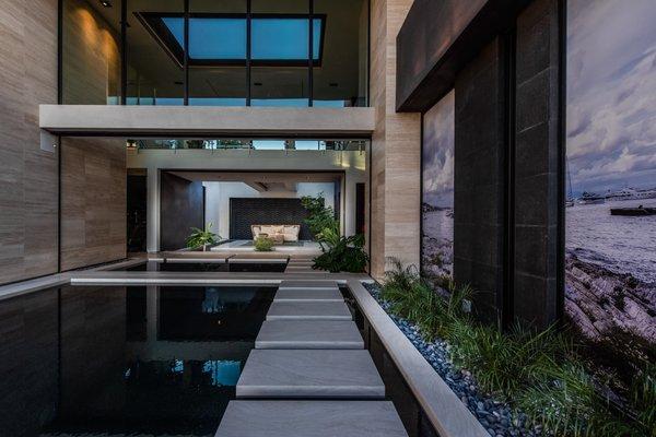 A stunning walkway surrounded by a pool accented by greenery and various types of stones.