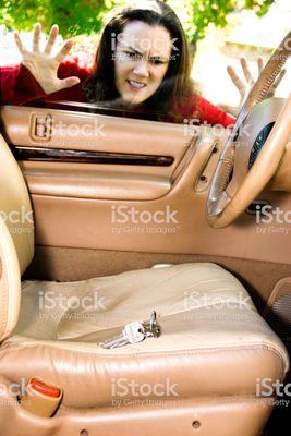 A woman looking in driver side of auto. Looking at auto keys locked in side of auto looking at the keys on set.