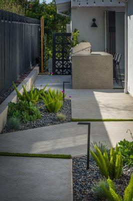 Side entrance with planters. Outdoor kitchen with concrete countertop that waterfalls on both sides. Breeze blocks painted black.