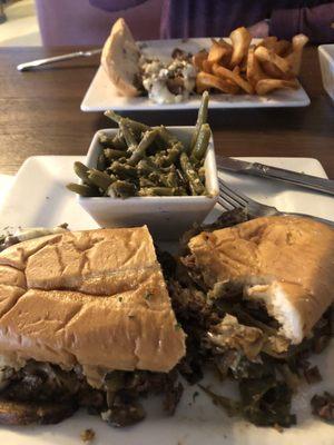 Philly Cheesesteak and green beans with breaded steak fries on other plate.