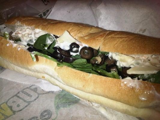 Seafood salad on Italian bread with spinach, black olives, green peppers and pepper check cheese.