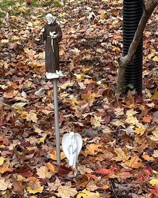 A small white religious figurine next to a Saint Francis statue in a fall garden.